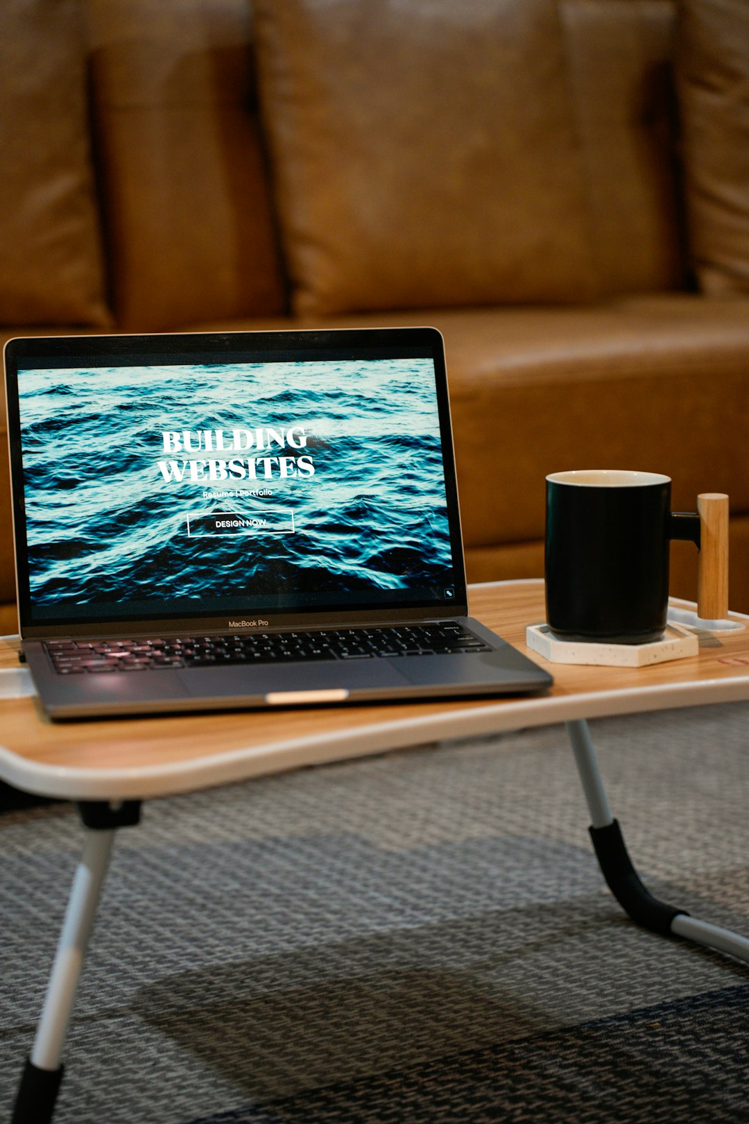 Build websites for your portfolio, resume, internal communications, wedding invitations, and more! A laptop, MacBook, on top of a portable table with coffee tea mug on the side.